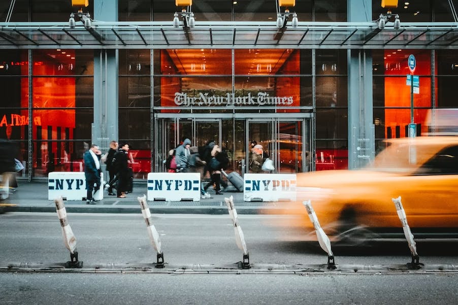 A photo of the New York Times office with a taxi passing in front.